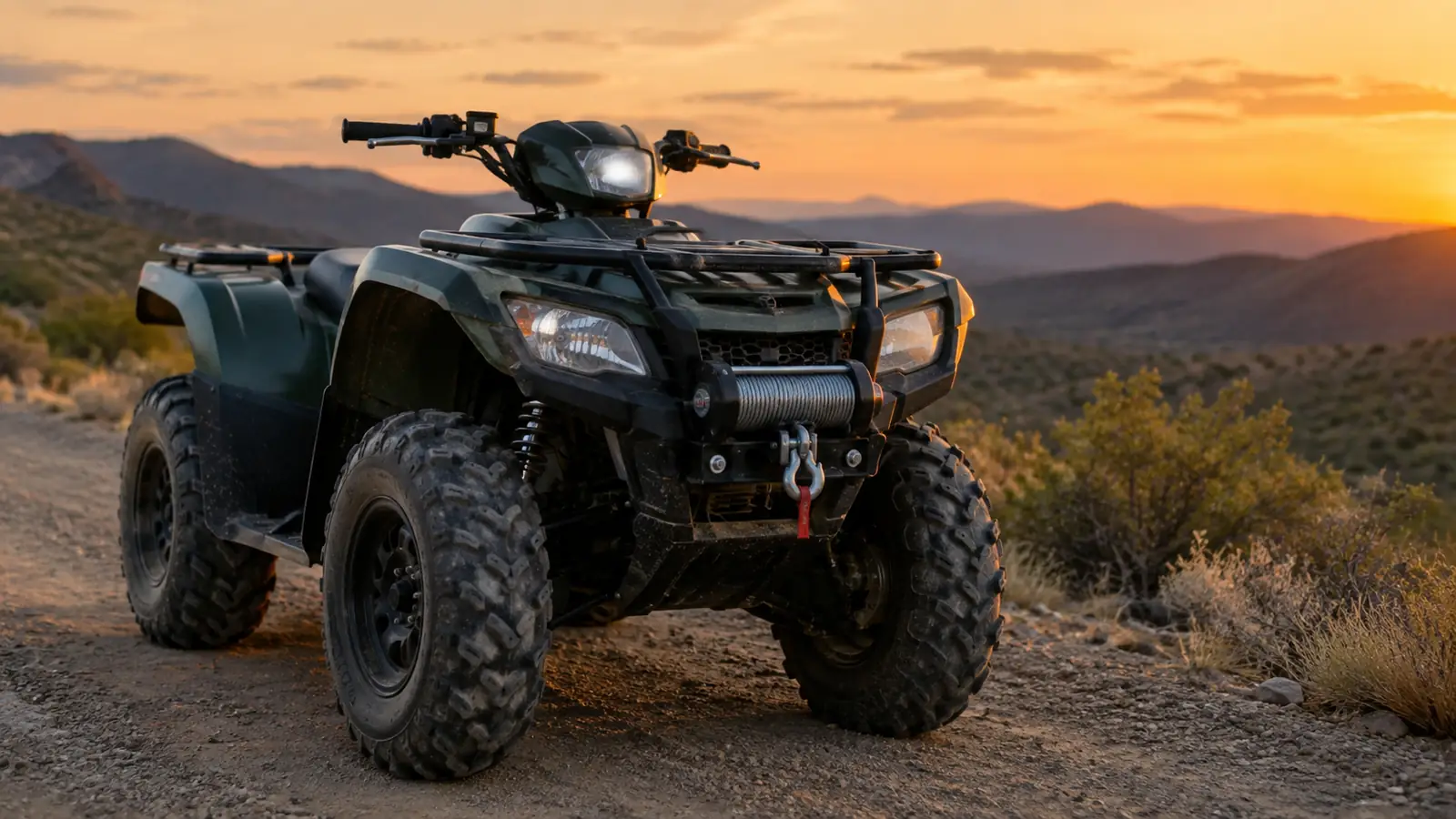 A quad parked on a fire road at dusk with a winch mounted on the front rack and cable spooled
