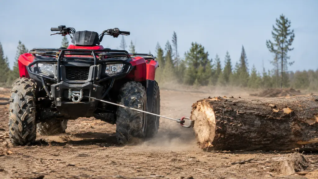 An ATV winching a heavy log across a dirt yard during a test pull