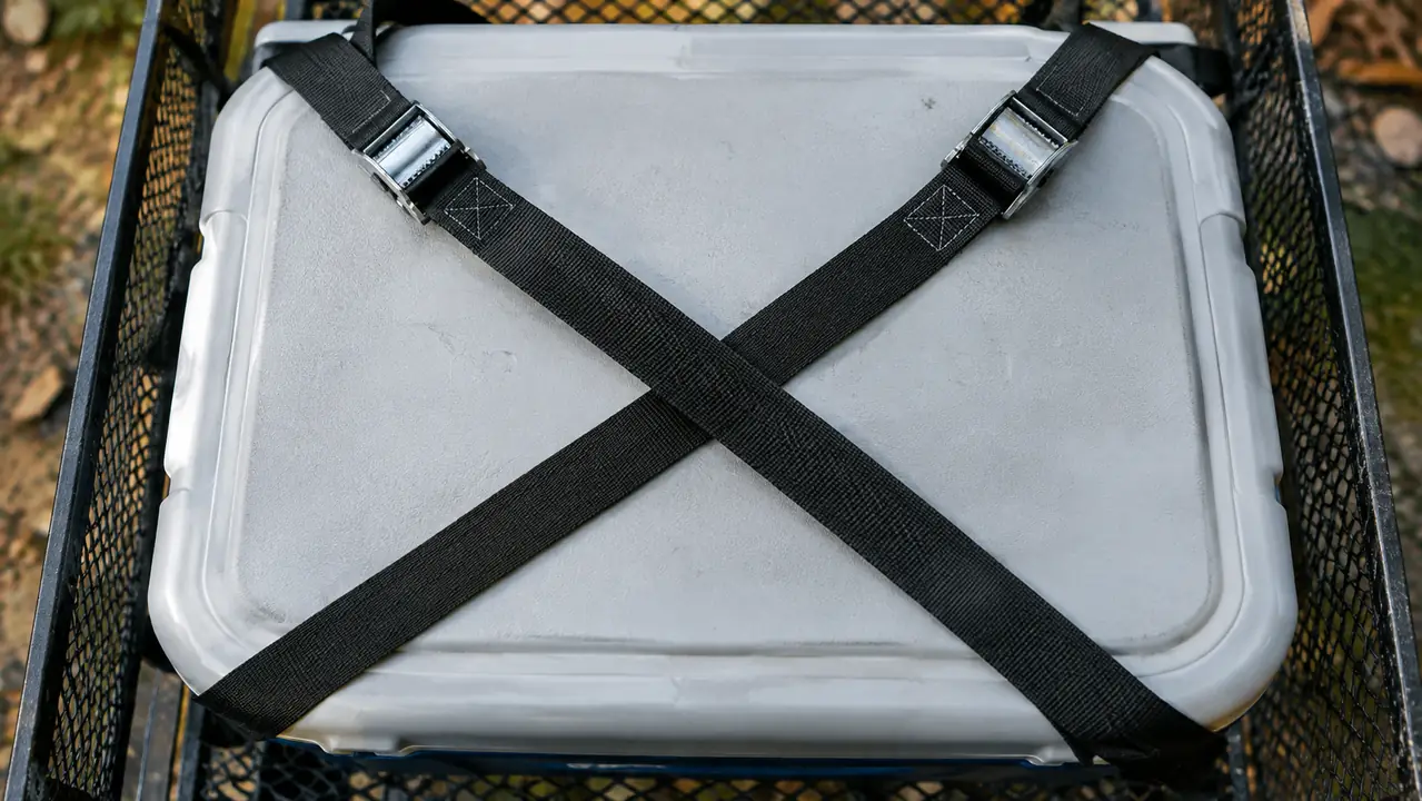 Two straps crossing in an X over the lid of a cooler in a steel cargo basket