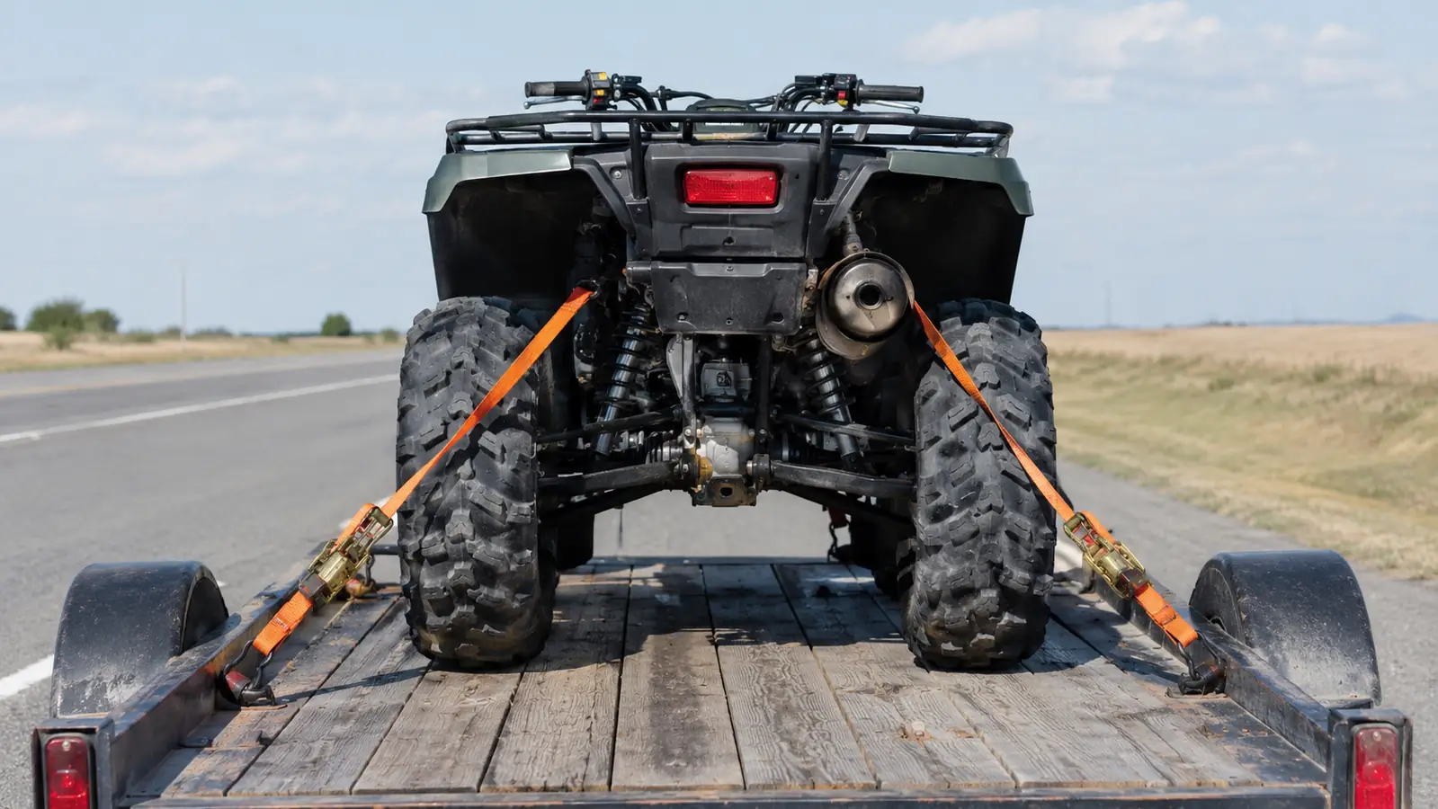 Rear view of a quad sitting level on a trailer with four tie-down straps running from the frame to the trailer corners