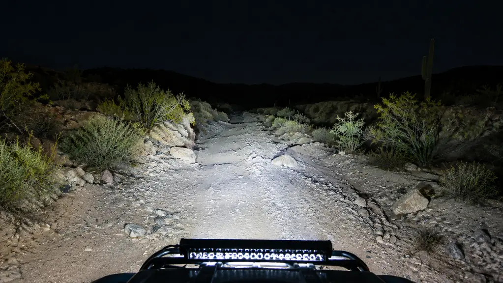 A desert wash at night illuminated by a wide beam from an ATV light bar