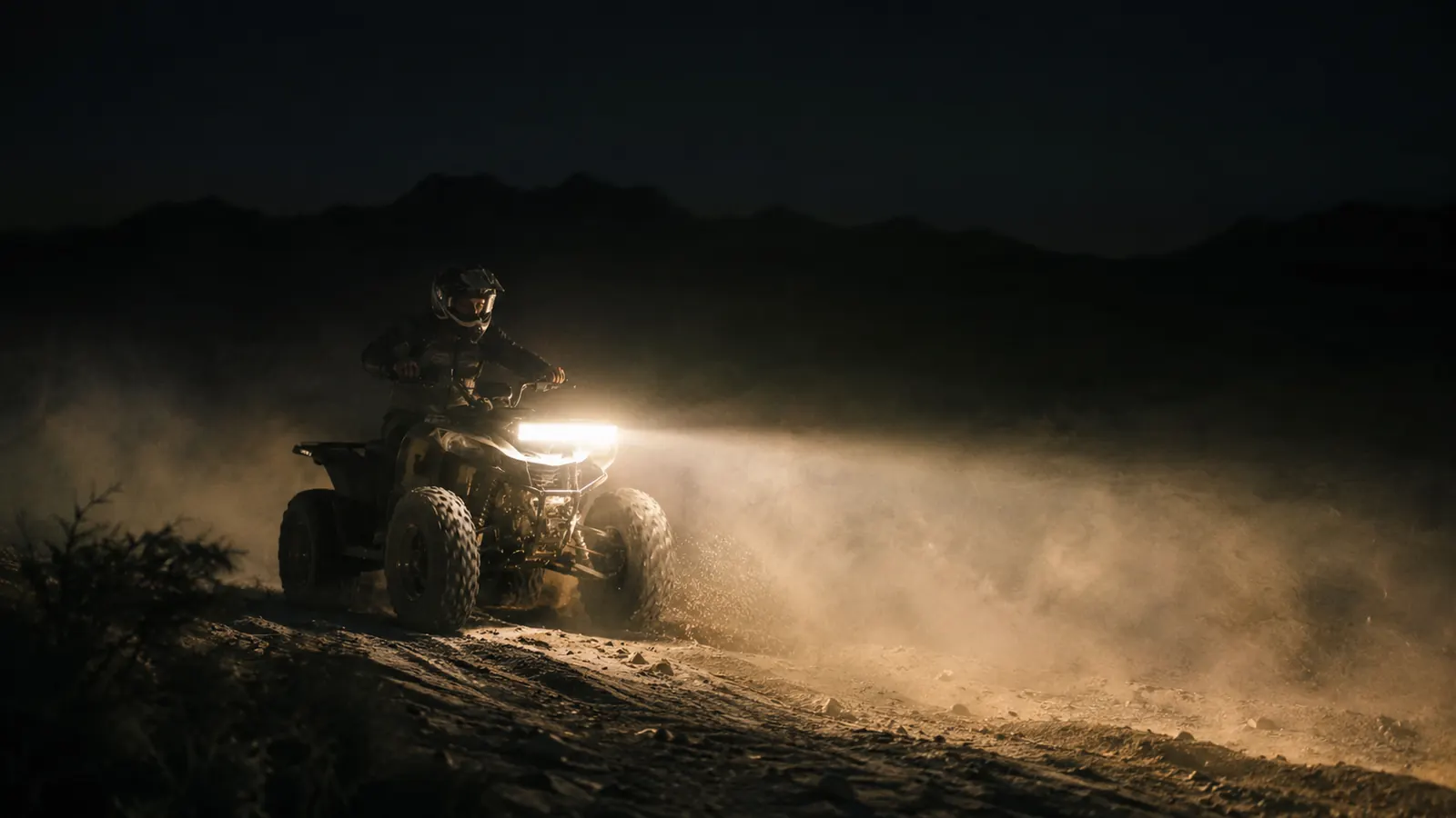 A quad driving on a dark desert trail at night with the light bar casting a wide beam ahead
