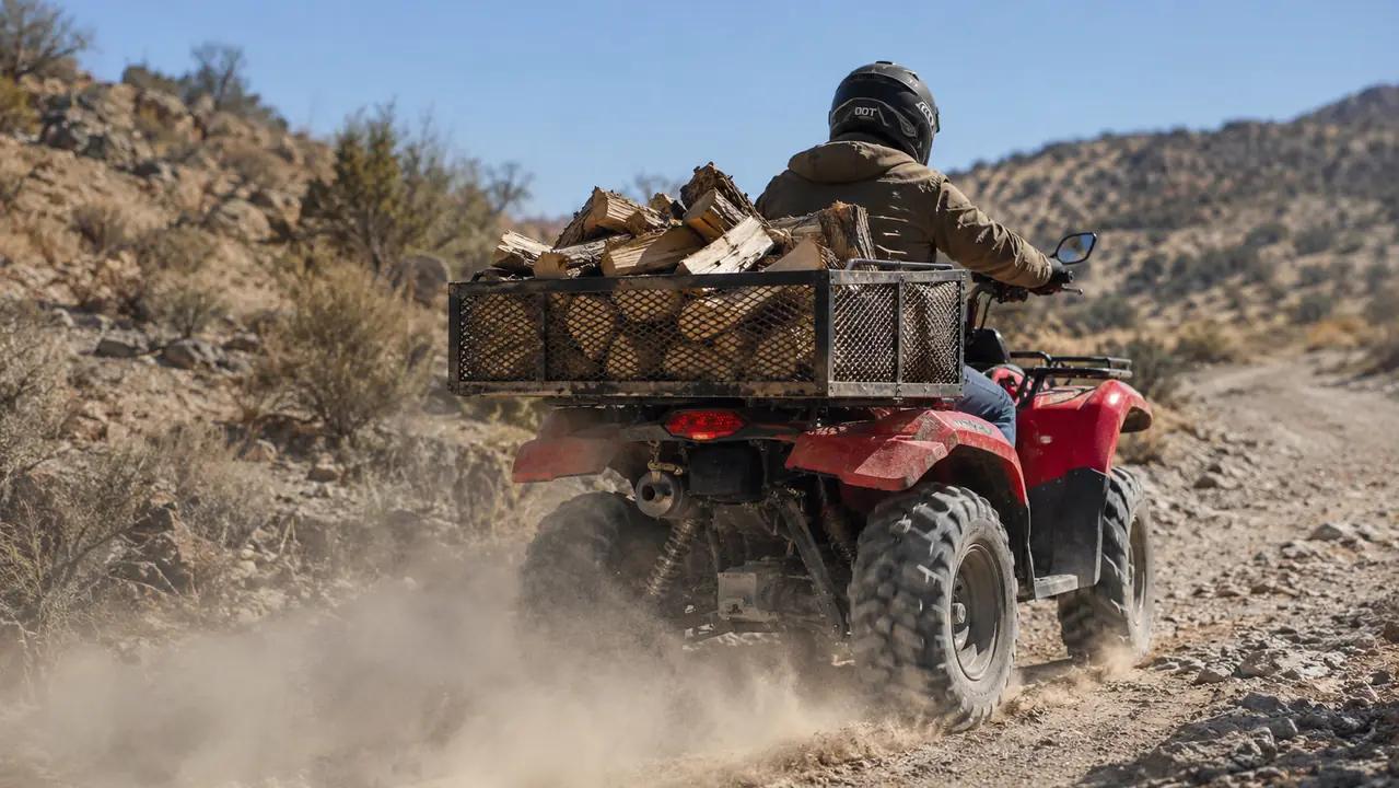 ATV on a rocky fire road with the rear steel mesh cargo basket loaded with split firewood and a dust trail behind